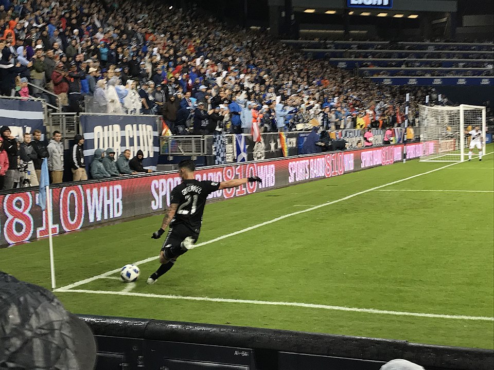Jugador ejecutando un saque de esquina en partido nocturno